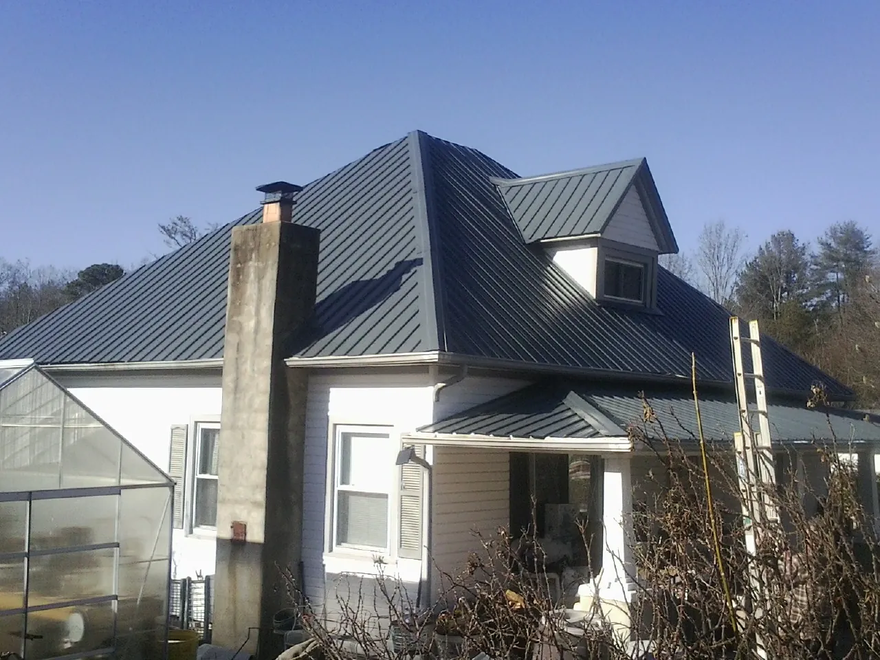 Dark blue standing seam metal roof on a white farmhouse with dormer — Slate & Tile Roof Repair by Roofing Brothers in Spring Branch