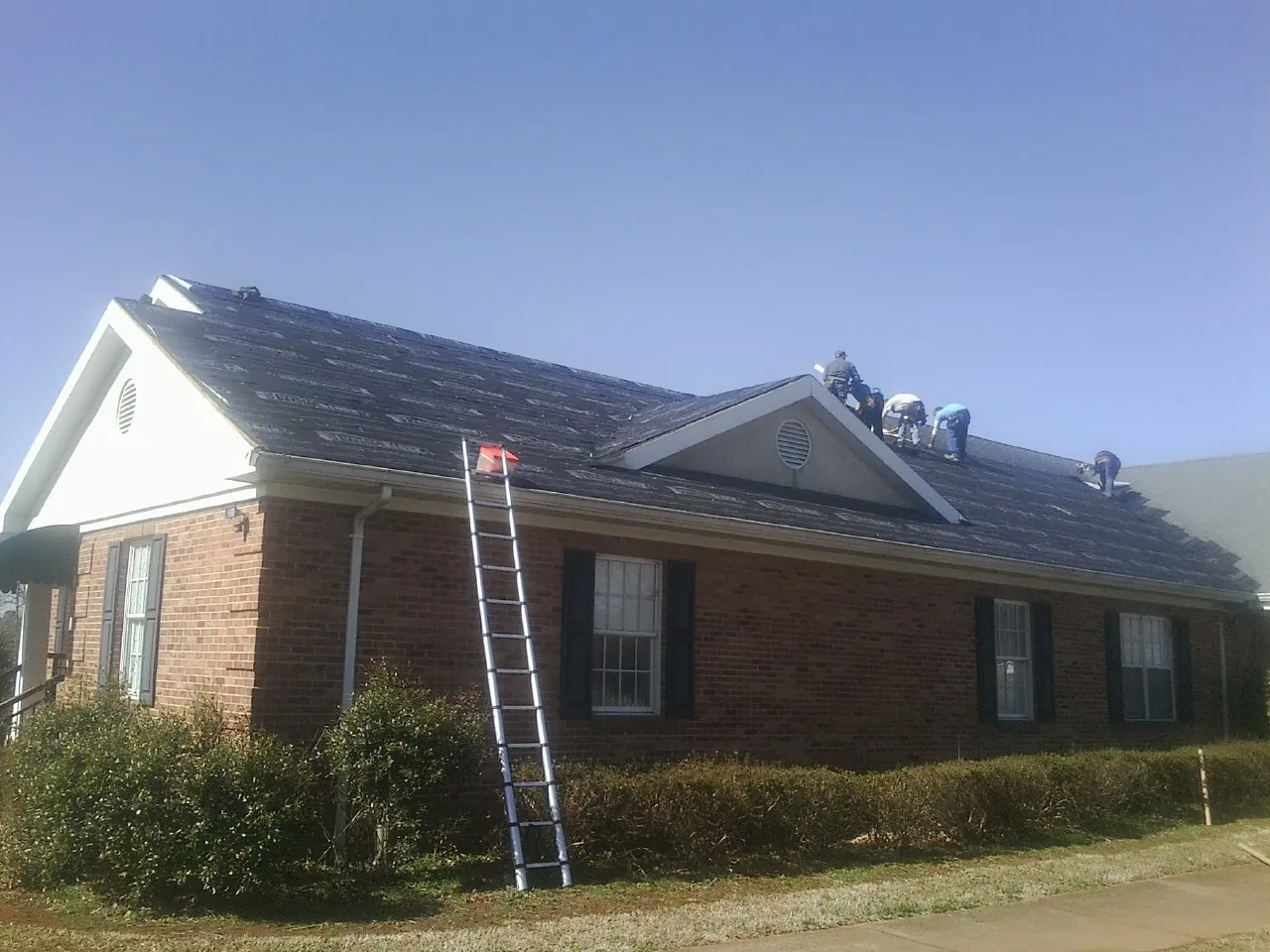 Crew tearing shingles off a brick ranch roof with a ladder set — Metal Roof Repair work by our crew in Spring Branch