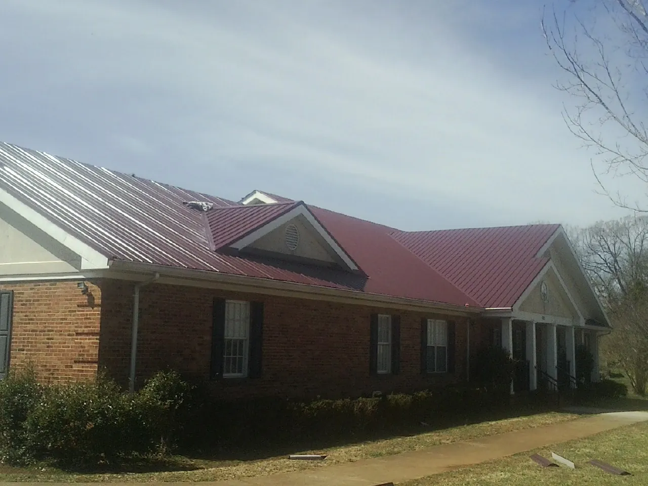 Red metal roof with gabled entries on a long brick building, from a Hail Damage Roof Repair job in Spring Branch