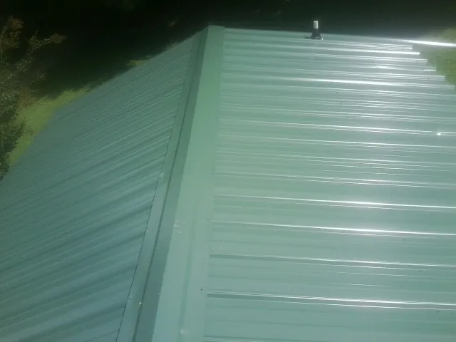 New green metal panels meeting at the ridge of a roof — Flat Roof Repair work by our crew in Spring Branch