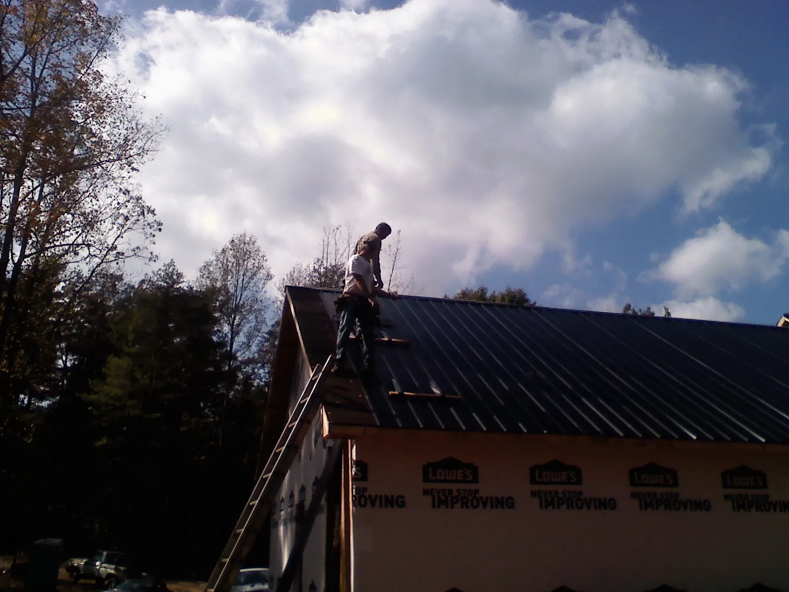 Roofer fastening dark metal panels high against a cloudy sky, from a Roof Inspection job in Spring Branch