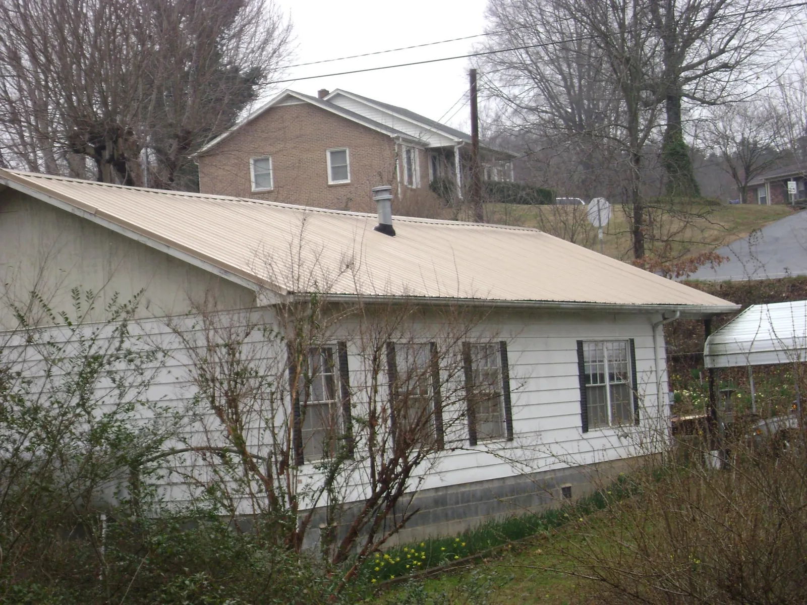 Tan metal roof on a white sided house set into a hillside — Commercial Roofing by Roofing Brothers in Spring Branch